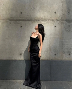 Woman in a black slip dress posing against a concrete wall in dramatic lighting