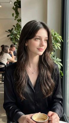 Woman with long dark hair holding a coffee cup in an indoor setting
