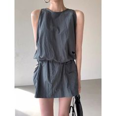 Woman in a gray sleeveless dress with a black bag and hoop earrings