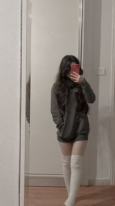 Person in a dark hoodie and white thigh-high socks taking a mirror selfie