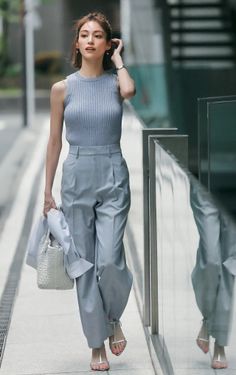 Woman in a light blue sleeveless top and wide leg pants walking outdoors
