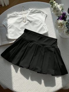 Black pleated skirt and white top with a pearl necklace on a table