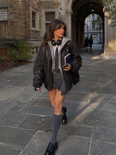 Woman in a school uniform and leather jacket walking on a college campus
