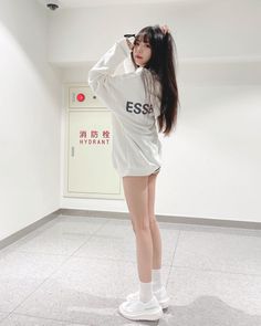 Woman in a white sweatshirt and white sneakers posing indoors