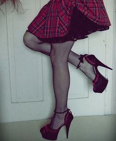 Person in fishnet stockings, plaid skirt, and platform heels posing indoors