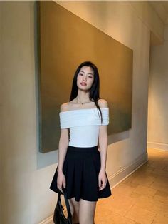 Woman with long black hair wearing an off-shoulder top and black skirt indoors