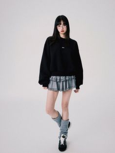 Woman with long black hair and glasses wearing a black sweatshirt and ruffle skirt