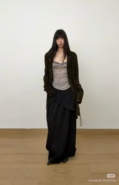 Woman with long dark hair wearing a dark coat and black skirt indoors