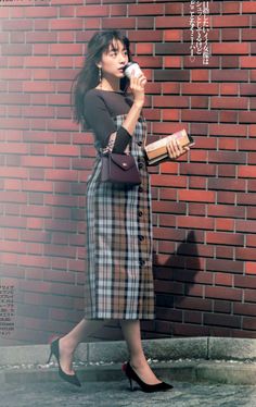 Woman in a plaid dress and high heels walking past a brick wall