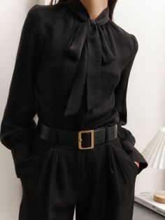 Person wearing a black pussy bow blouse and black pants with a wide belt