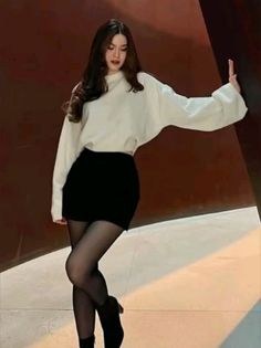 Woman with long hair wearing a white sweater and black skirt with tights indoors