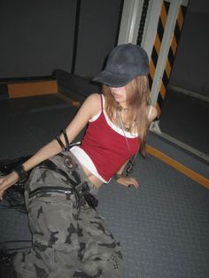 Woman in a red tank top and camo pants with a baseball cap indoors