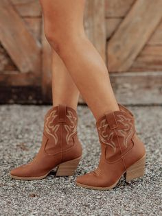 Person wearing brown cowboy boots with embroidered details on a gravel ground