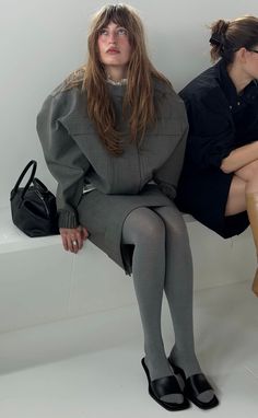 Woman with long hair in a gray outfit and tights sitting indoors