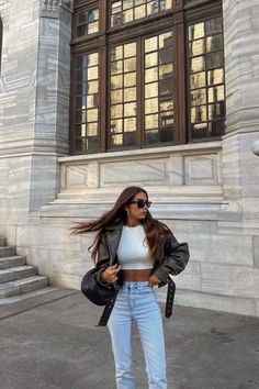 Woman in a leather jacket and crop top standing outdoors
