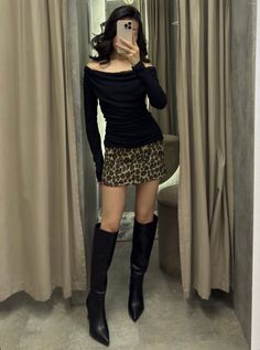 Woman in a leopard print skirt and black off-shoulder top taking a mirror selfie