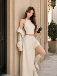 Woman in a cream crop top and skirt with a long coat and boots outdoors