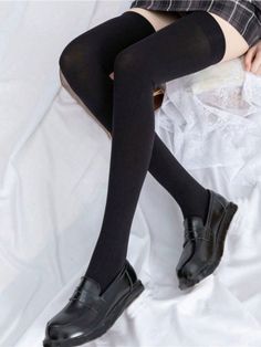 Person wearing thigh high socks, a plaid skirt, and black shoes on white bedding
