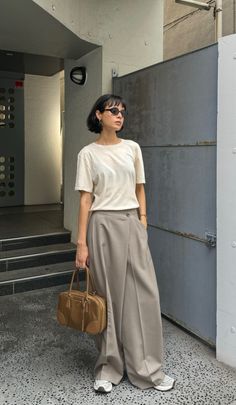 Woman with short hair and sunglasses holding a brown handbag outdoors