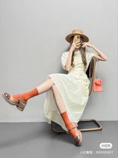 Person in a straw hat and white dress sitting on a chair, holding a phone
