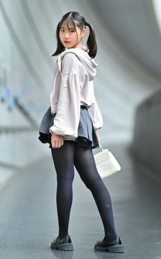 Young woman with pigtails wearing a hoodie, pleated skirt, and black tights