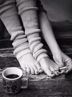 Person painting toenails while wearing leg warmers, with a coffee cup nearby