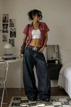Woman in a plaid shirt, crop top, and baggy jeans with a skull belt indoors