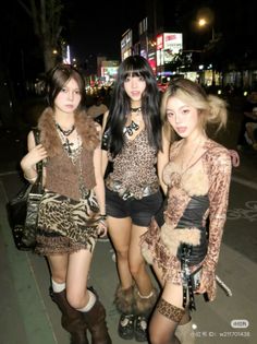 Three women in leopard print and fur trim outfits on a street at night