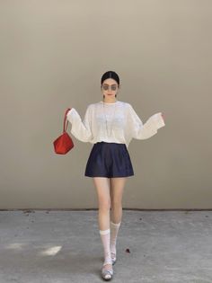 Woman in sunglasses and a white top holding a red handbag, standing outdoors