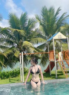Woman in a black bikini in a swimming pool with palm trees in the background