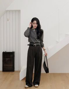 Woman in a gray cardigan and wide leg pants holding a black handbag indoors