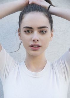 Woman with dark hair in a bun and a white shirt, looking directly at the camera