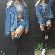 Person in a denim jacket, crop top, denim shorts, and fishnet stockings against a black wall