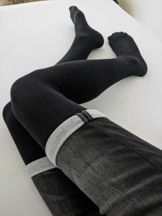 Person wearing black socks and cuffed black jeans on a white surface