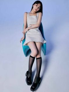 Woman in a crop top and mini skirt with knee-high socks sitting on a chair