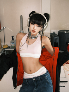 Woman with space buns and headphones wearing a crop top and jeans indoors