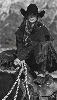 Woman in a cowboy hat and fringed jacket crouching on a horse's saddle