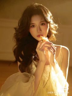 Woman with long hair in a lace dress holding a flower with soft, warm lighting