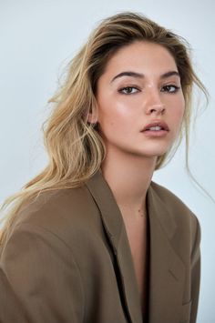 Woman with blonde hair wearing a brown blazer, looking directly at the camera