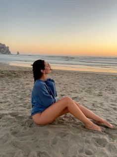 Woman in a blue sweatshirt sitting on a beach at sunset