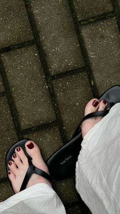 Feet with red nail polish wearing black sandals on paved ground