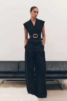 Woman in a black sleeveless top and wide-leg pants with a belt indoors