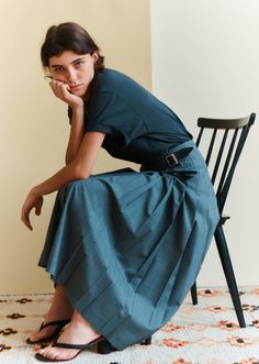 Woman with dark hair and blue eyes sitting on a chair in a t-shirt and midi skirt