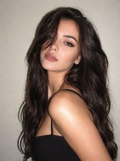 Woman with long dark wavy hair wearing a black top, looking at the camera