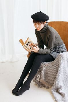 Woman in a beret and turtleneck reading a book while sitting in a chair
