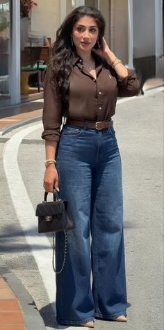 Woman in a brown shirt and wide leg jeans holding a handbag outdoors
