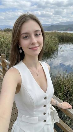Woman in a white vest and jewelry on a wooden bridge by a lake
