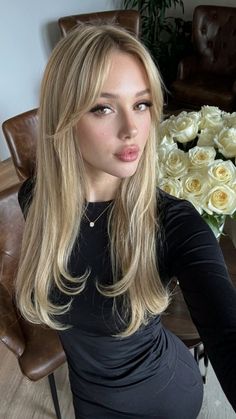 Woman with long blonde hair and a black dress, with white roses in the background
