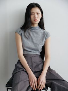 Woman with long black hair wearing a gray top and wide leg pants, sitting indoors