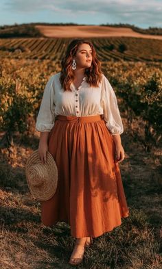 Woman in a white blouse and long skirt holding a straw hat in a vineyard